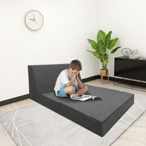 Boy reading on a gray folding sofa in a modern living room.