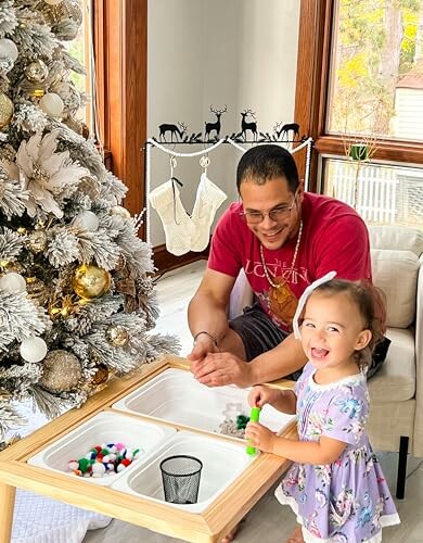 Father and daughter enjoying a Christmas activity by the tree.