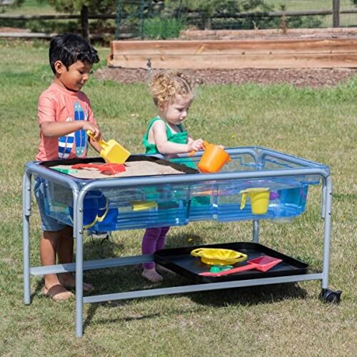 Two children playing with a sand and water table outdoors.